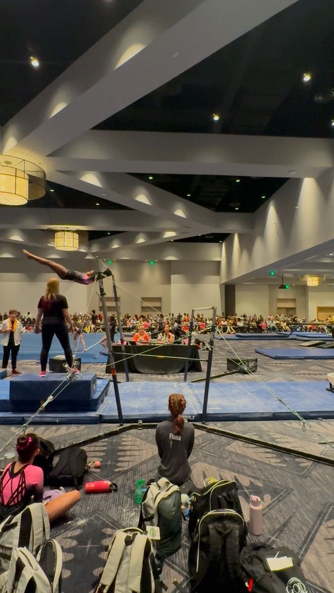 Gymnast on uneven bars performing a routine, large crowd watching in a convention hall.