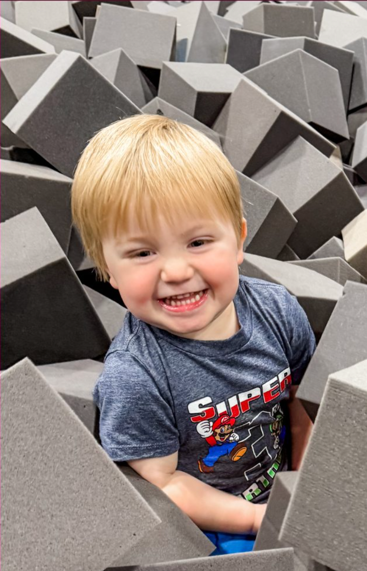 Girl with bun hairstyle climbs an indoor rock wall, focusing on handholds, with a rope.