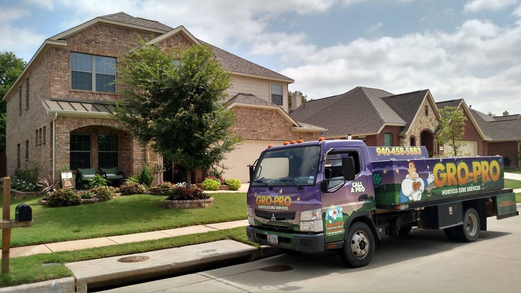 A Gro-Pro truck parked in front of a brick house with a well-manicured lawn.
