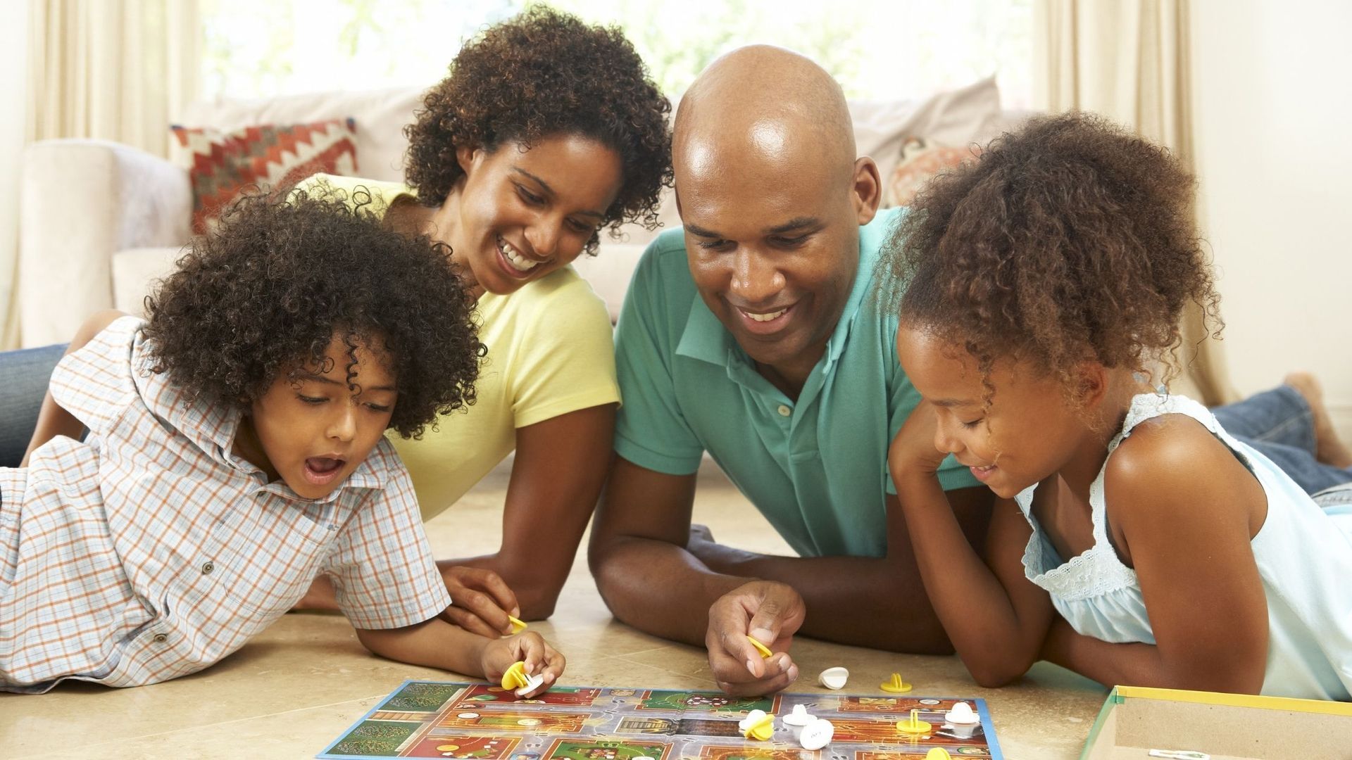 Family playing a board game on a wooden floor, smiling and focused.