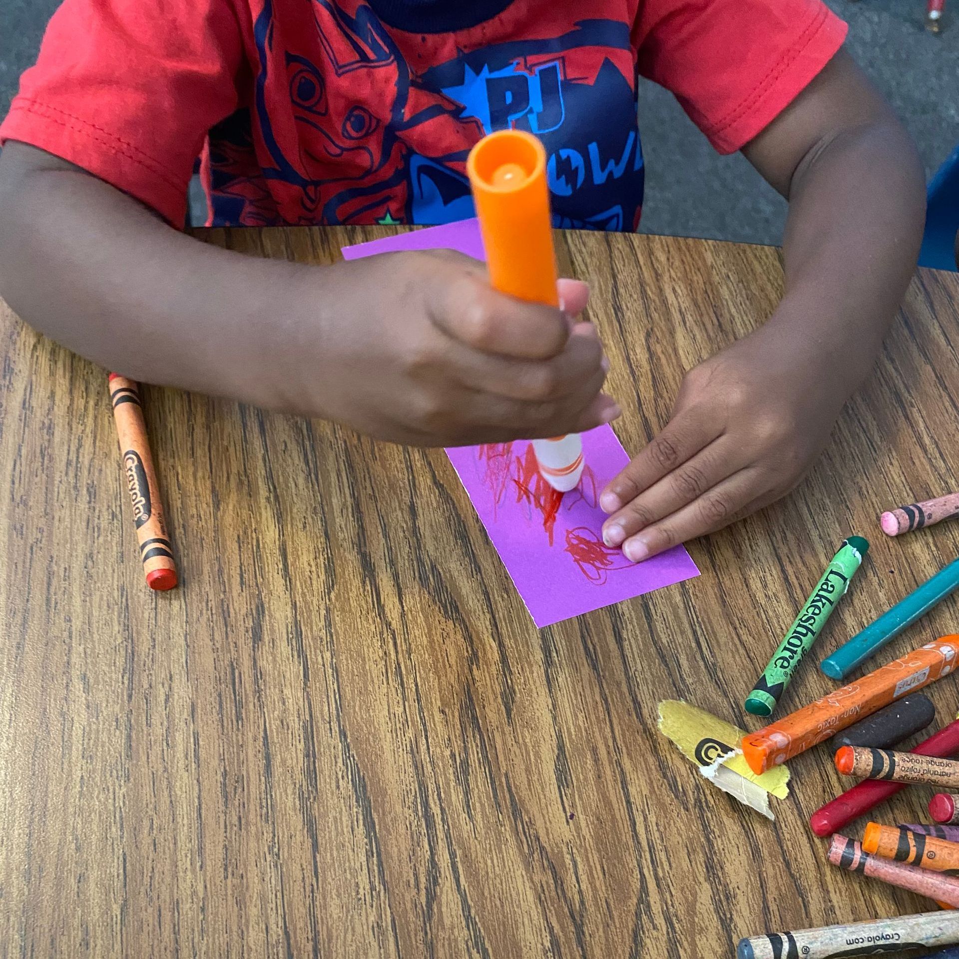 A child is drawing on a piece of paper with a marker that says crayola