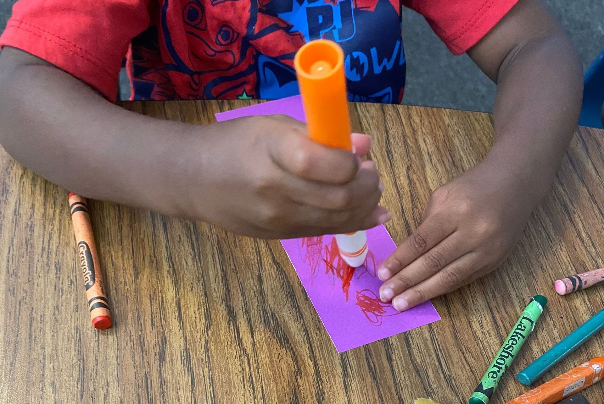 A child is sitting at a table with crayons and glue.
