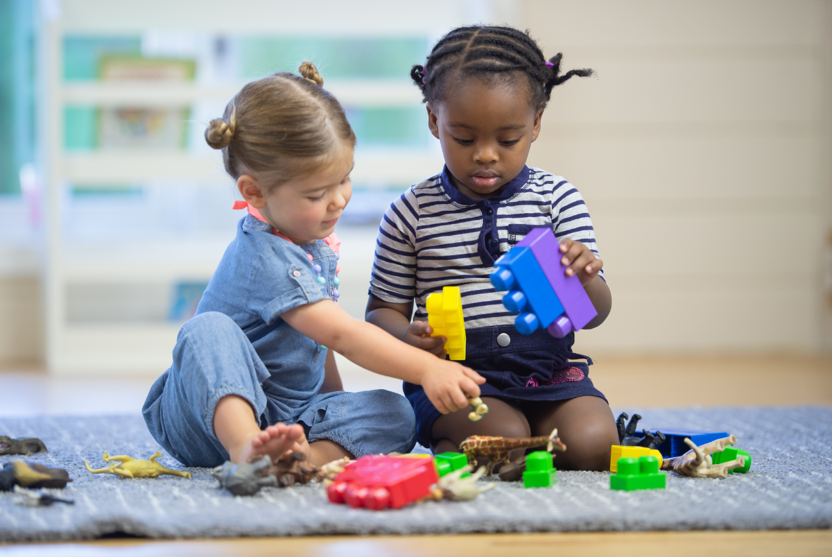 Two little girls are sitting on the floor playing with toys.