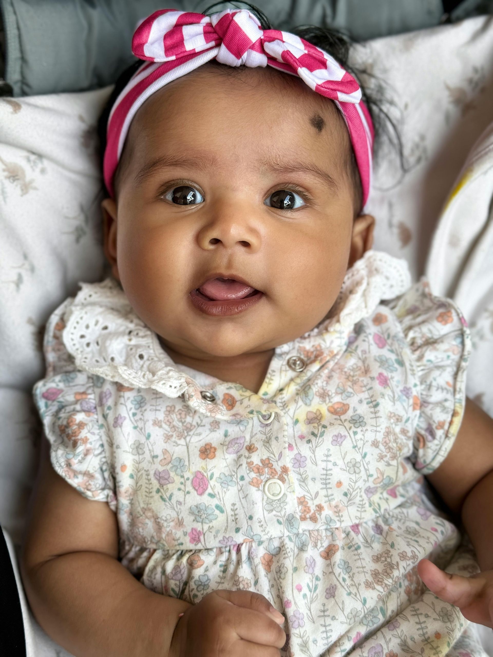 Woman working on laptop, holding baby; kitchen setting, smiles.