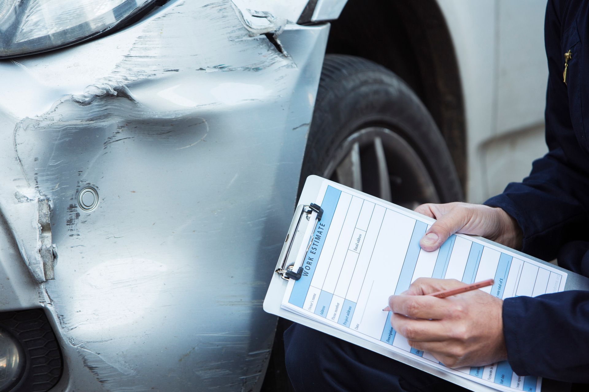 a man is sitting in front of a damaged car and writing on a clipboard .