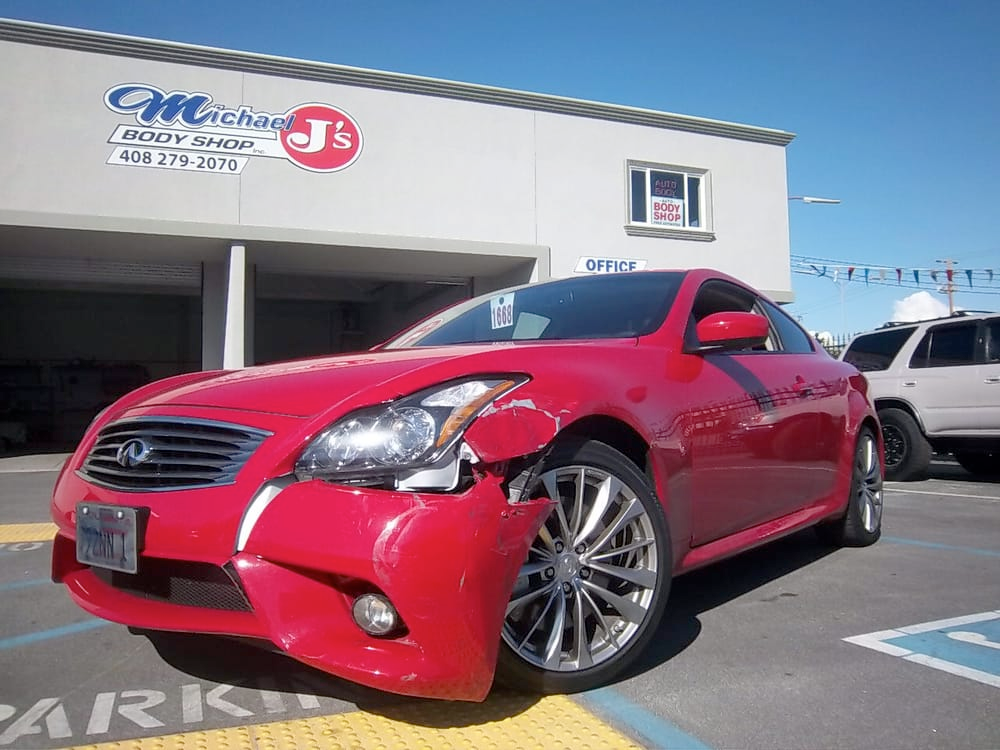 a red car with a damaged bumper is parked in front of a car dealership
