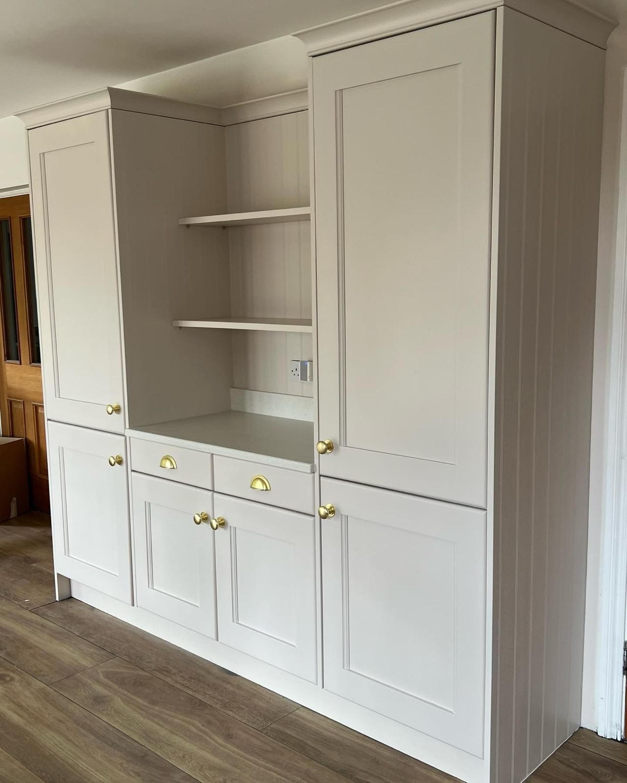 a large white cabinet with gold handles and shelves in a room .