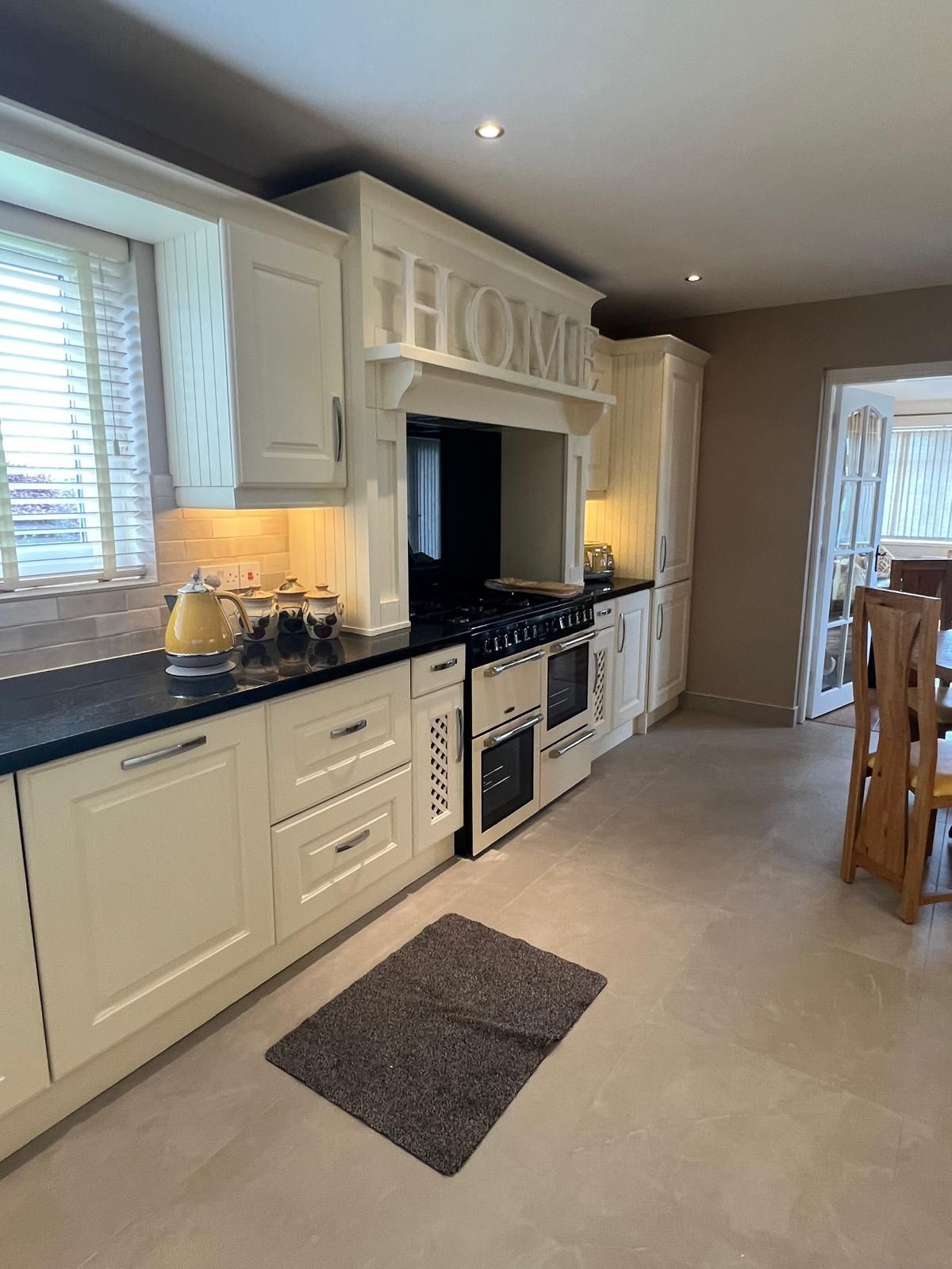 A kitchen with white cabinets , black counter tops , a stove and a rug on the floor.