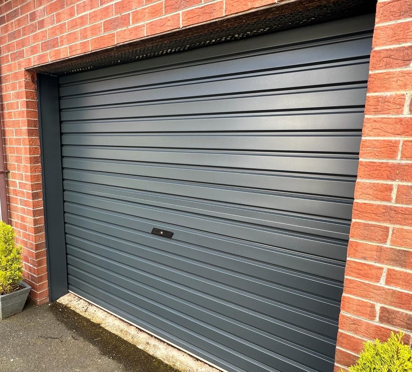 a black garage door is sitting in front of a brick building .