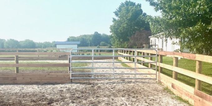 A wooden fence with a metal gate in the middle of a dirt field.