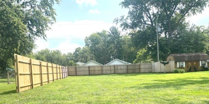 A wooden fence surrounds a large lush green field.