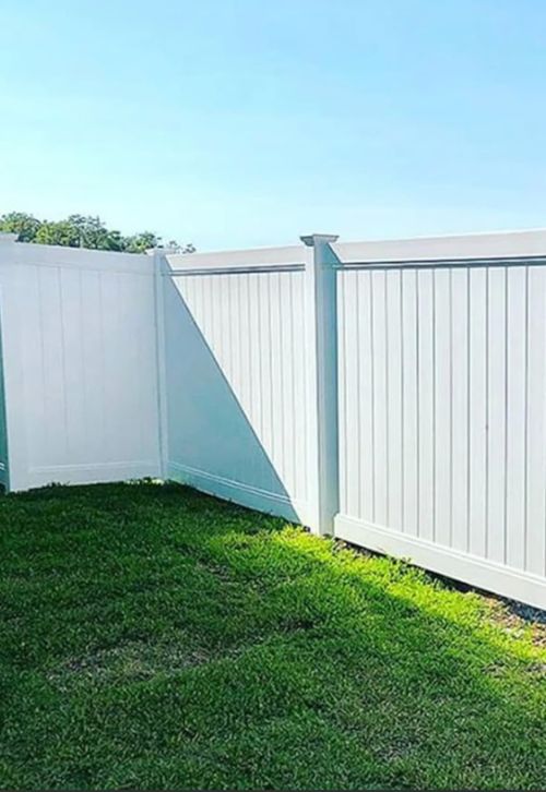 A white vinyl fence is sitting on top of a lush green lawn.