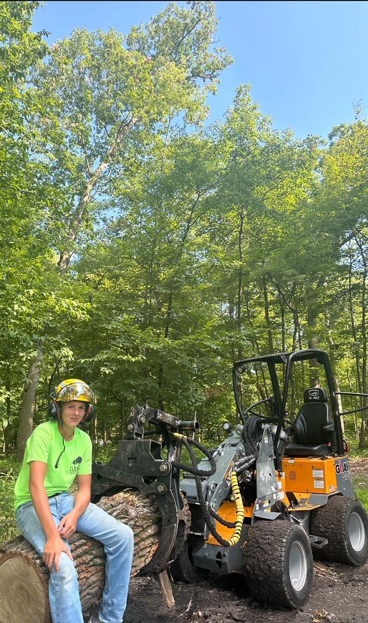 A man is sitting on a log next to a bulldozer in the woods.
