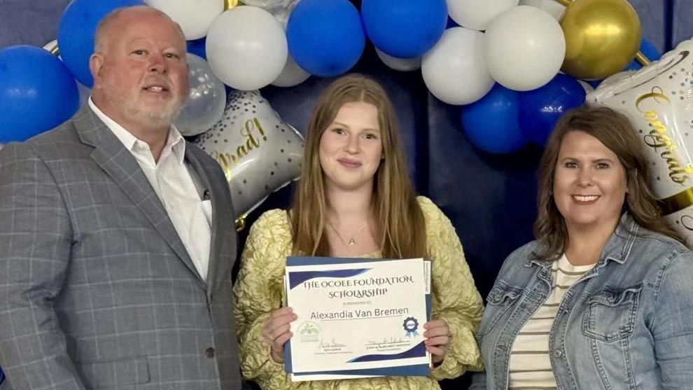 A woman is holding a certificate while standing next to a man and a woman.