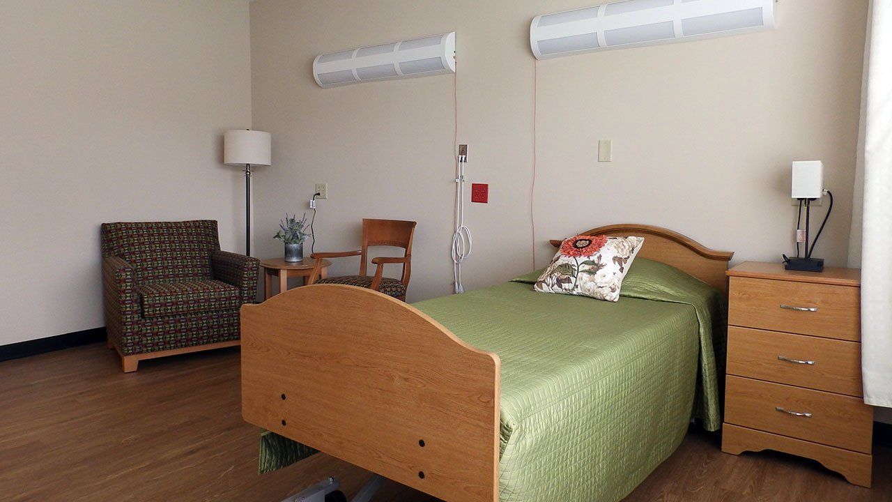A hospital room with a bed , chair , nightstand and lamp