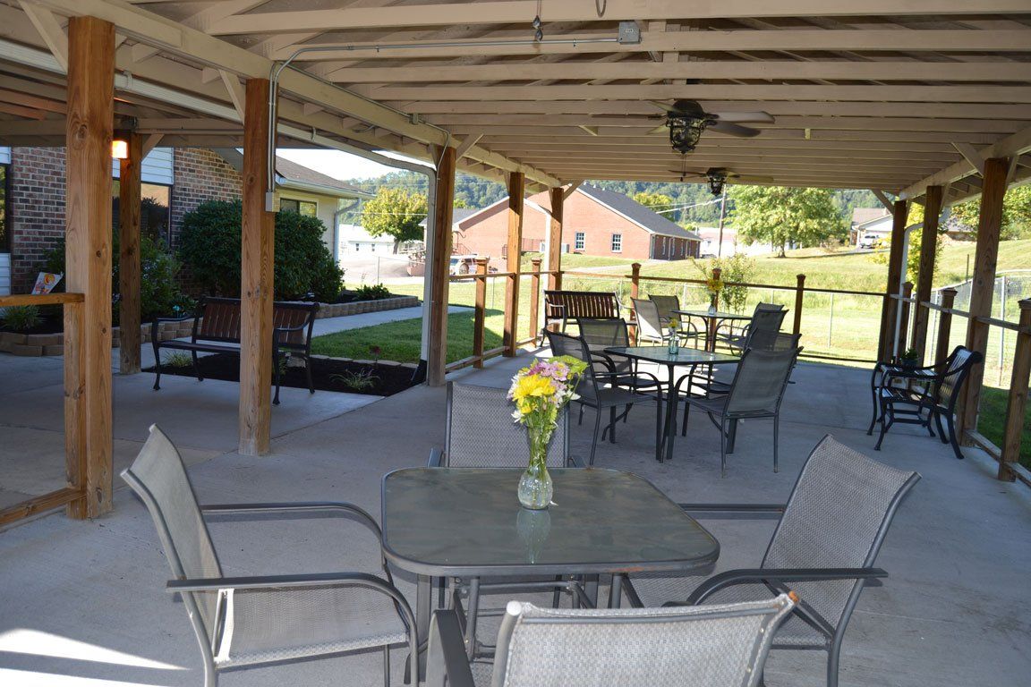 A table and chairs under a covered patio with a vase of flowers on it.