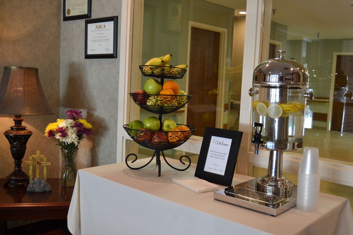 A table with a fruit stand and a drink dispenser on it.