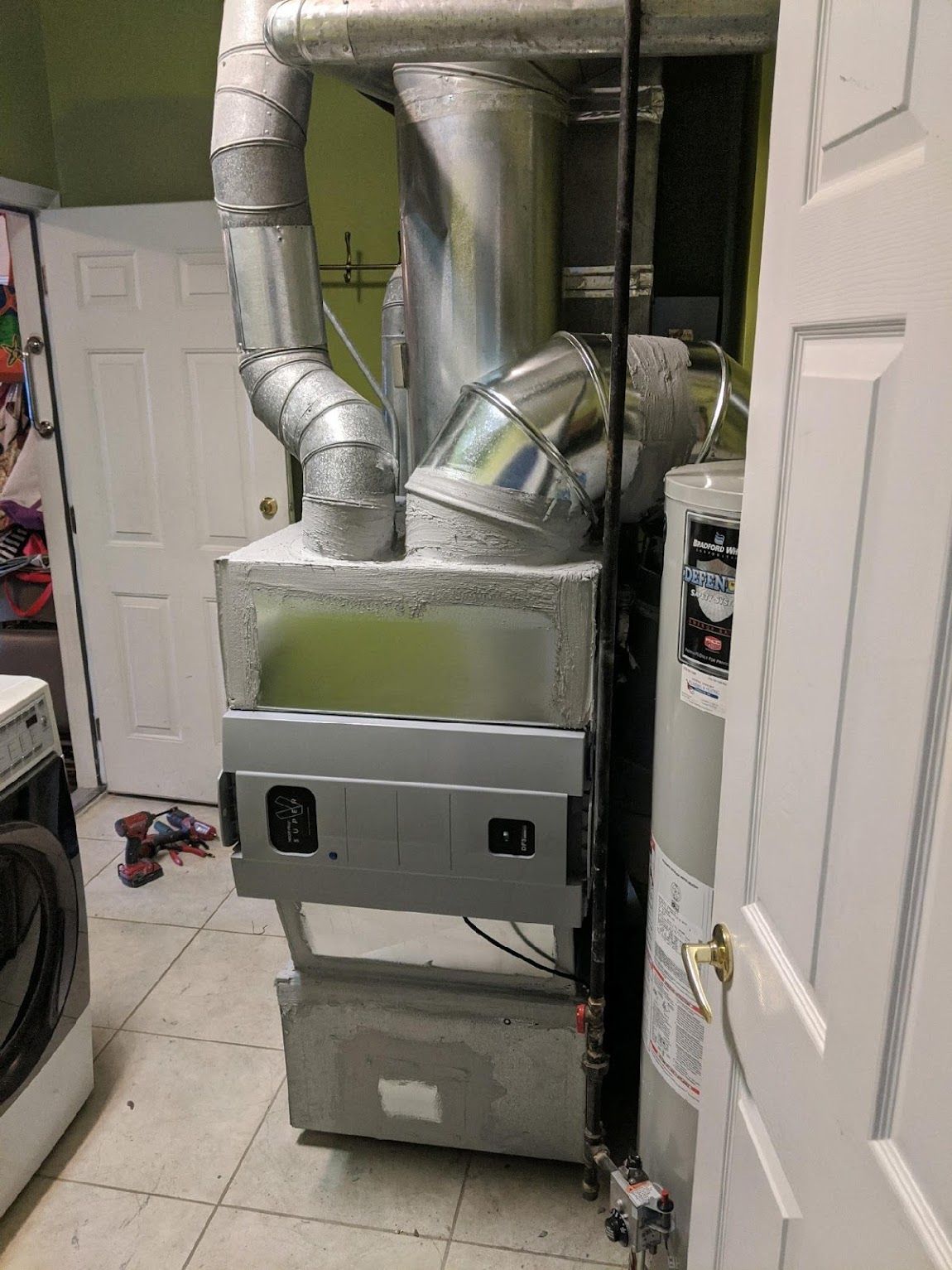 A furnace unit with metal ductwork in a utility room next to a water heater and a washing machine.