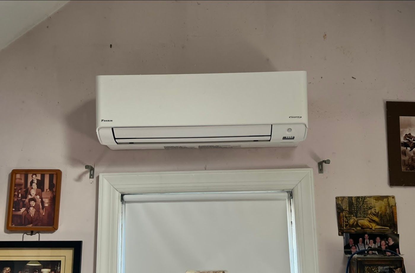 A white, rectangular air conditioning unit mounted on a light-colored wall above a window frame.