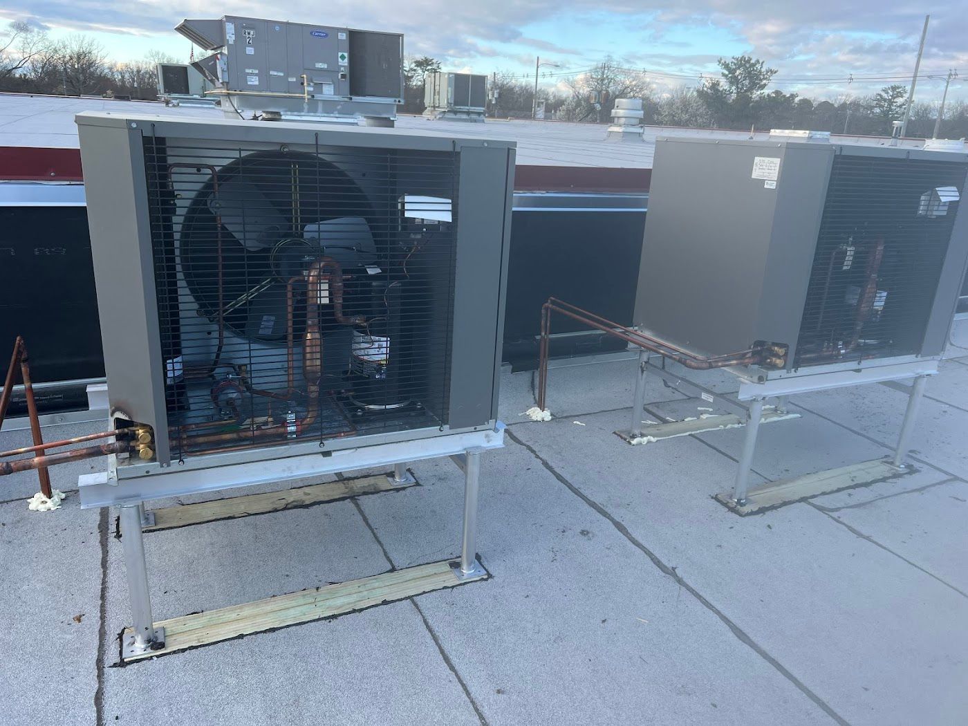 Two HVAC condenser units on a flat, light-gray industrial roof under a bright, cloudy sky.