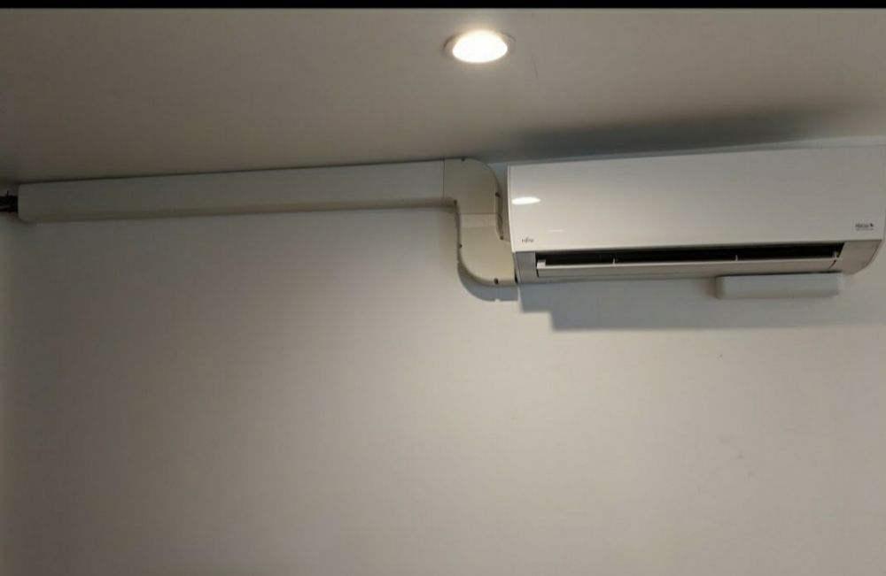 A white wall-mounted air conditioning unit with white trunking running horizontally along the wall above it.