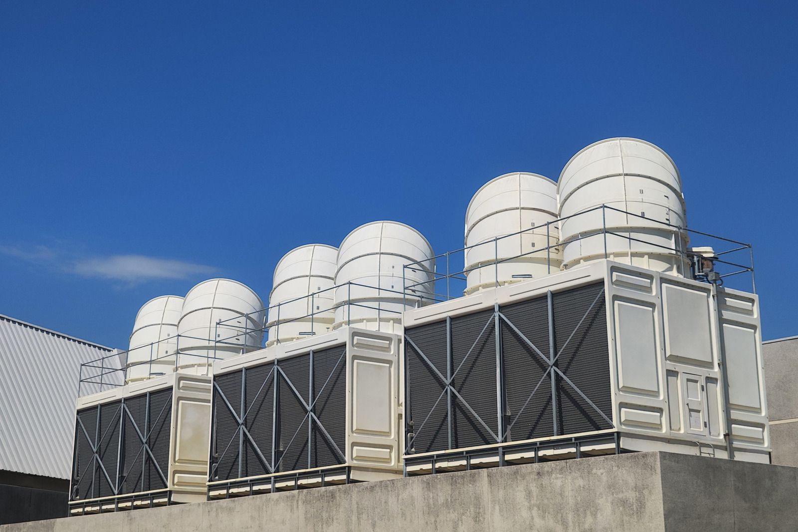A row of industrial cooling towers with large white fans on a rooftop against a clear blue sky.