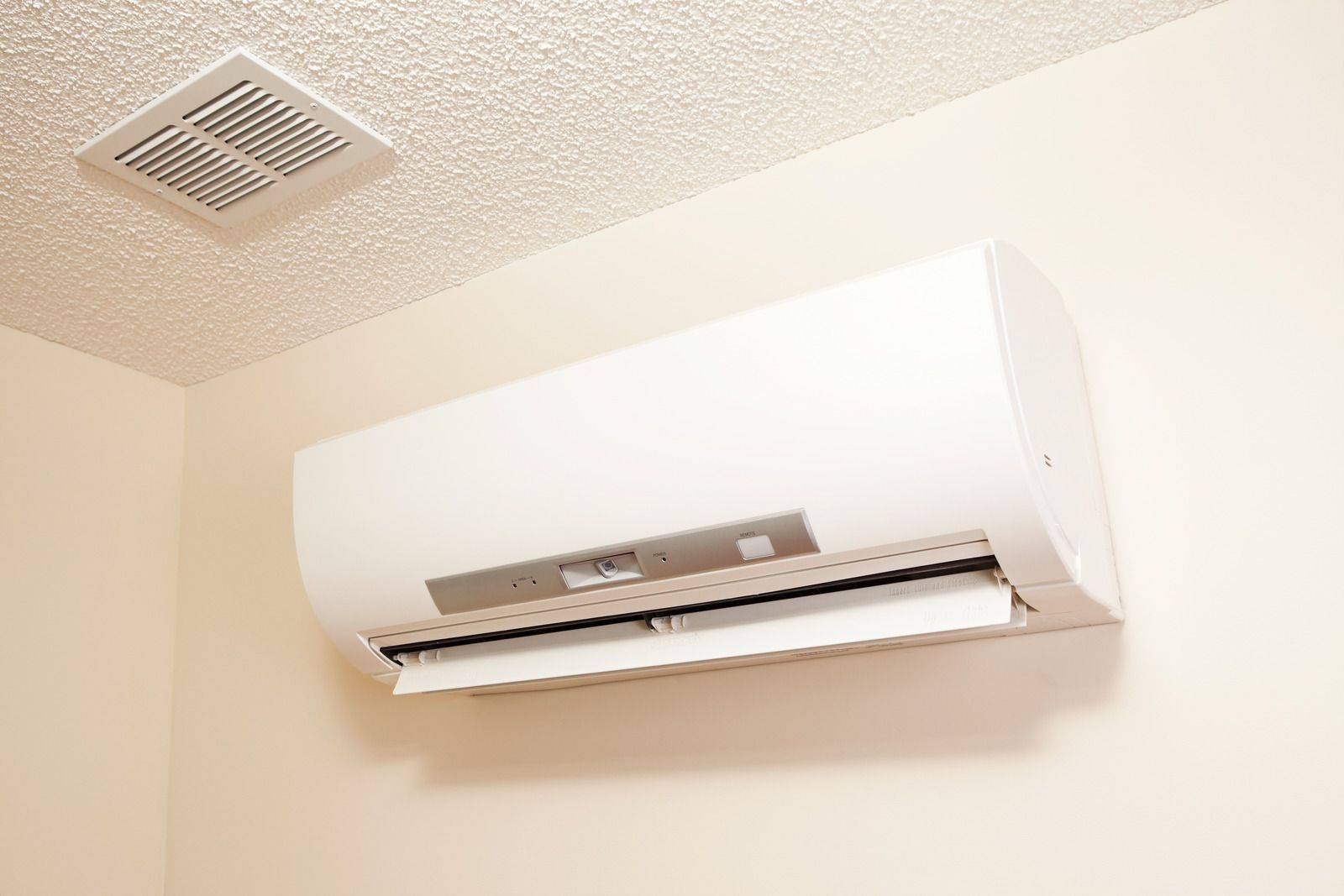 A white wall-mounted air conditioning unit installed on a cream-colored wall below a ceiling vent.
