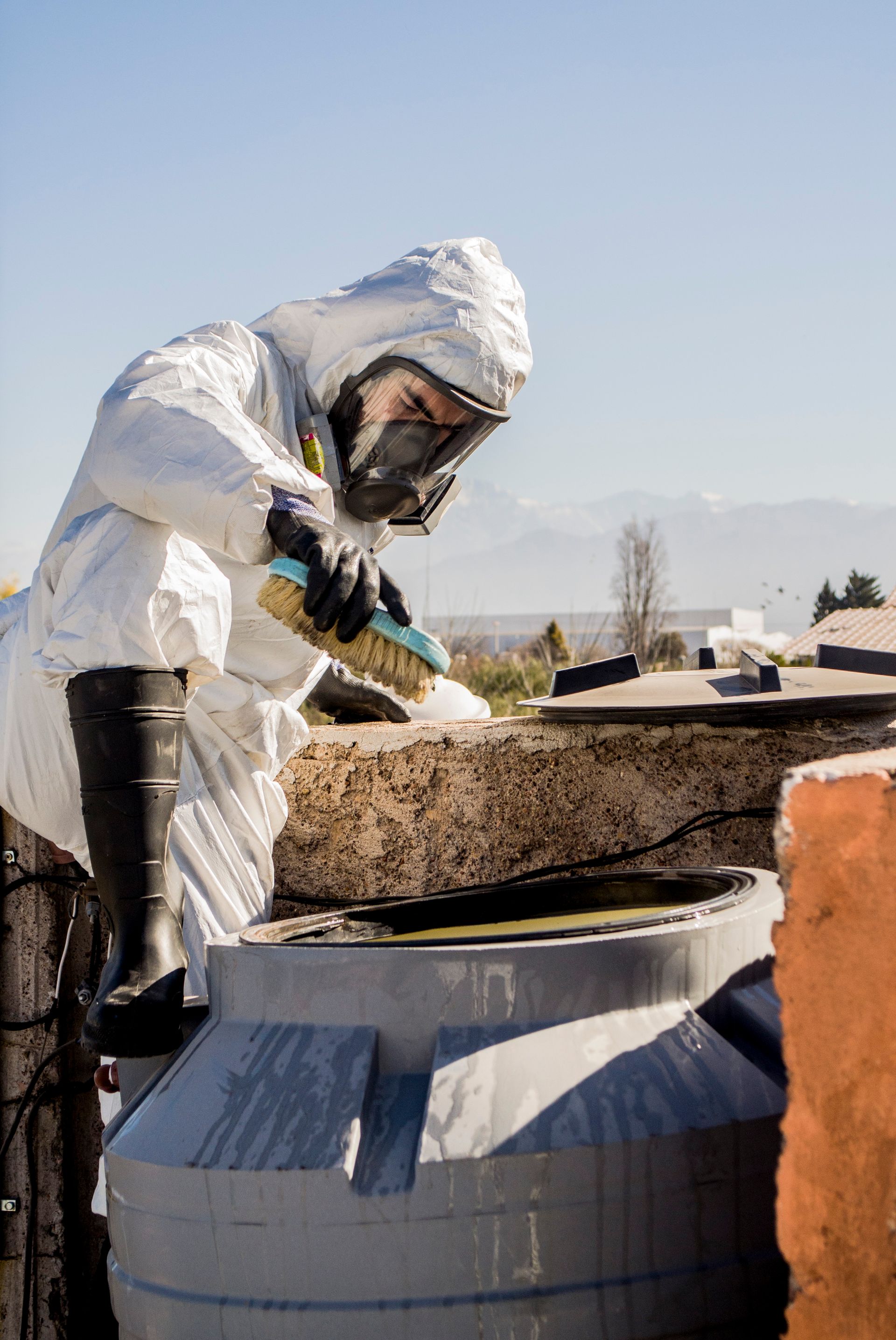 Una persona con traje de materiales peligrosos limpia los escombros de un contenedor al aire libre.