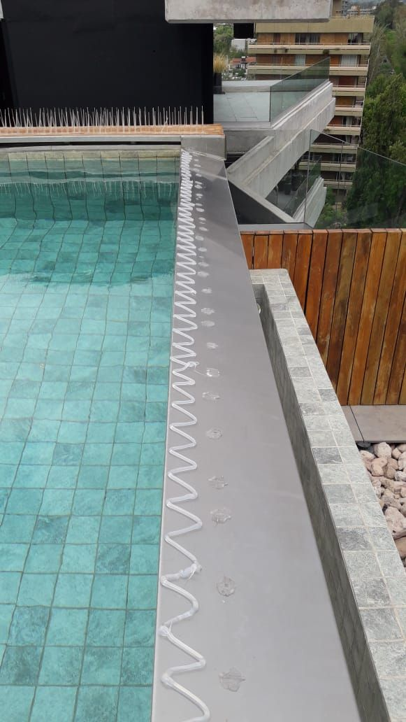 Borde de la piscina con azulejos verde azulado. Borde metálico largo con sellador blanco.