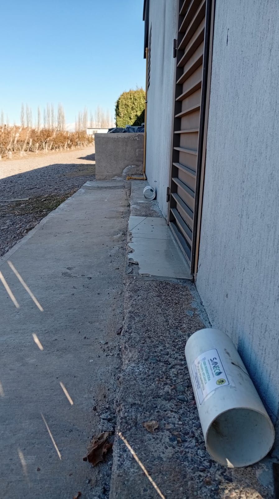 Pasarela de hormigón al lado de un edificio con una puerta de rejilla cerrada; un trozo de tubo de PVC blanco