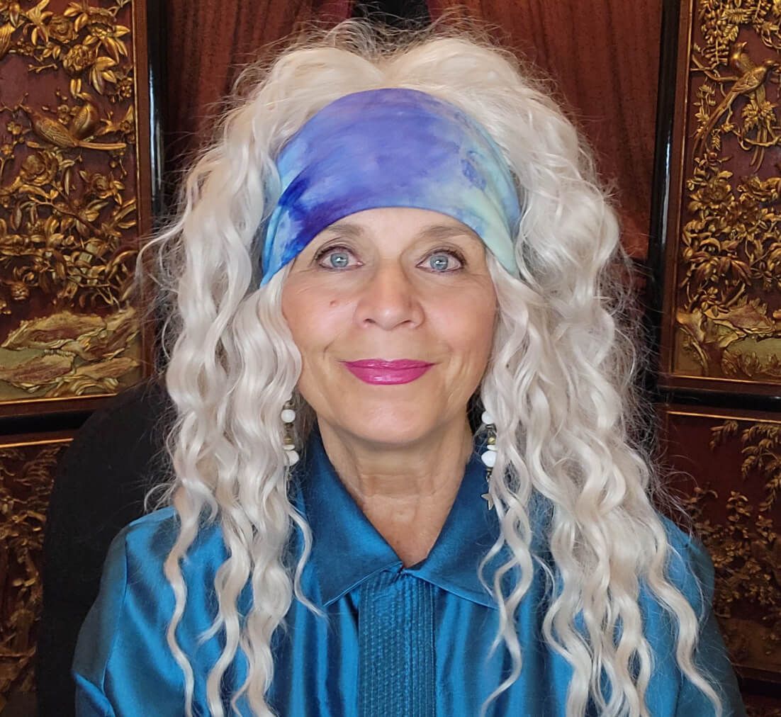 A woman with long white hair is wearing a blue shirt and a purple headband.