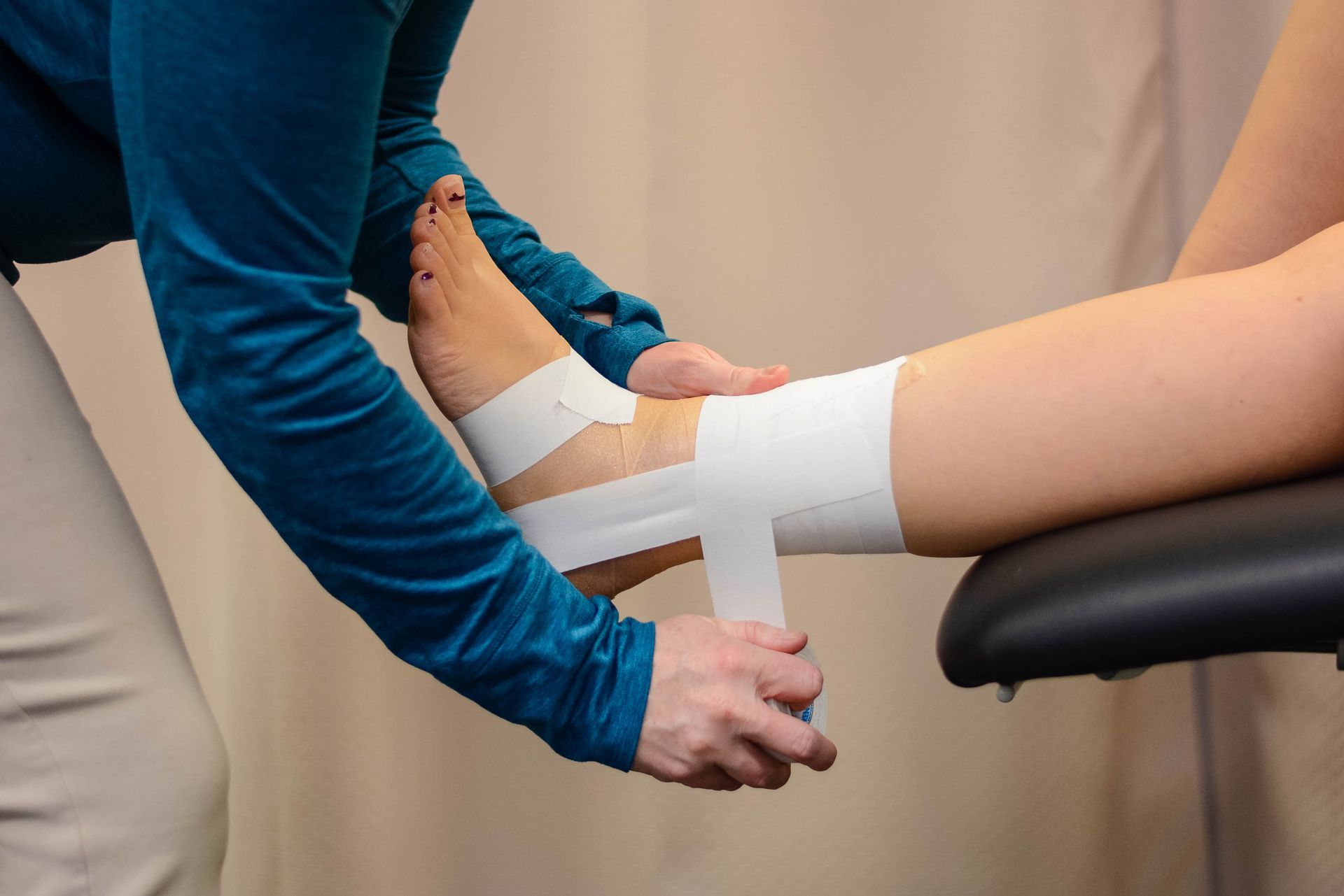 Person wrapping white athletic tape around another person's ankle.