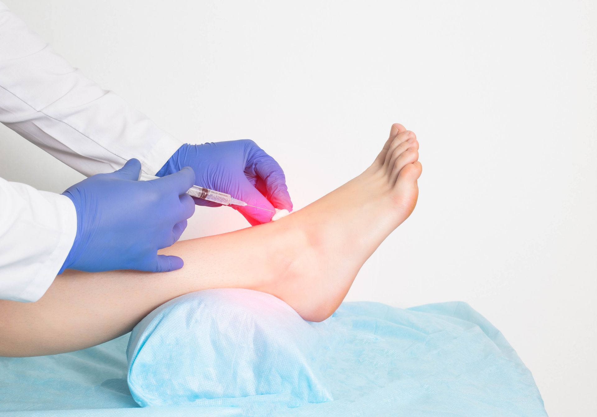 Doctor administering an injection into a patient's foot; highlight shows pain, light blue setting.