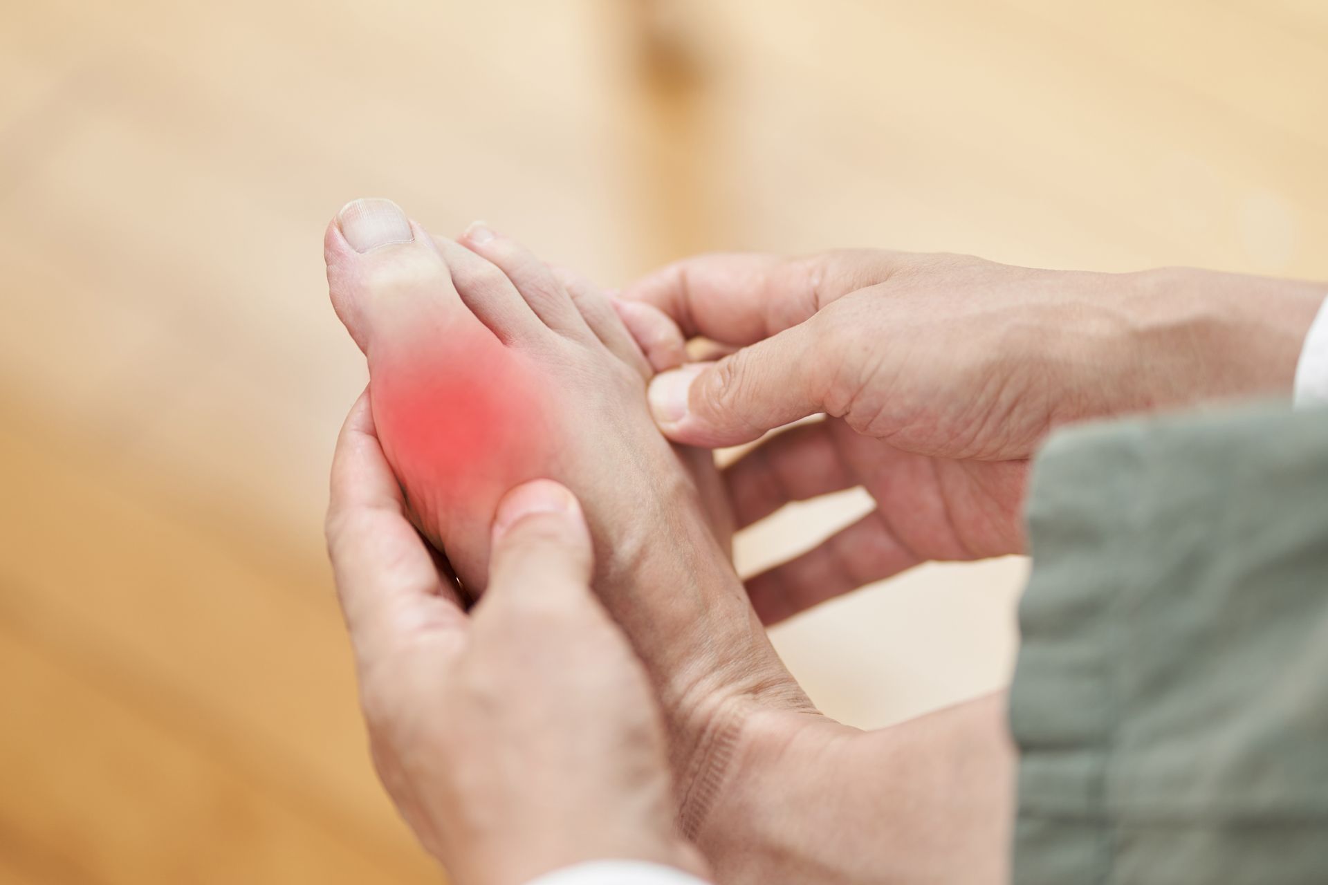 Person holding foot, red area indicating pain near big toe, possibly gout.