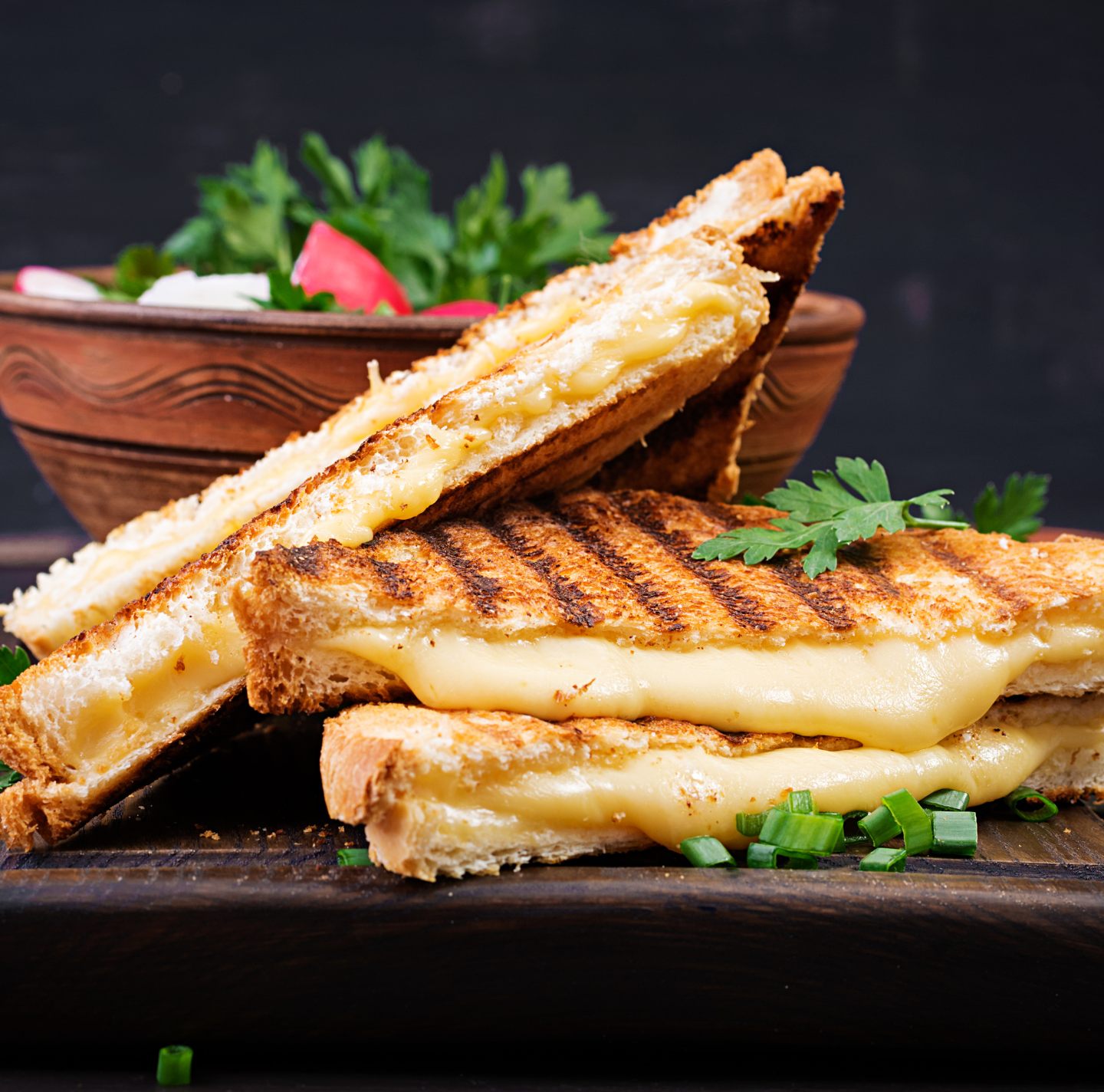 Two grilled cheese sandwiches are stacked on top of each other on a wooden cutting board.