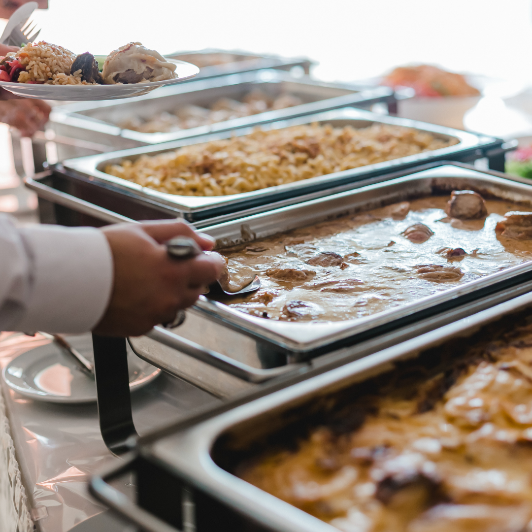 A person is taking a tray of food from a buffet line.