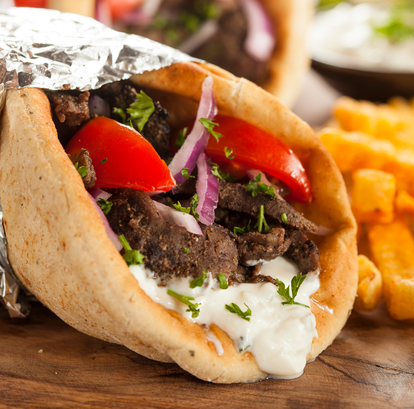 A close up of a gyro with french fries in the background