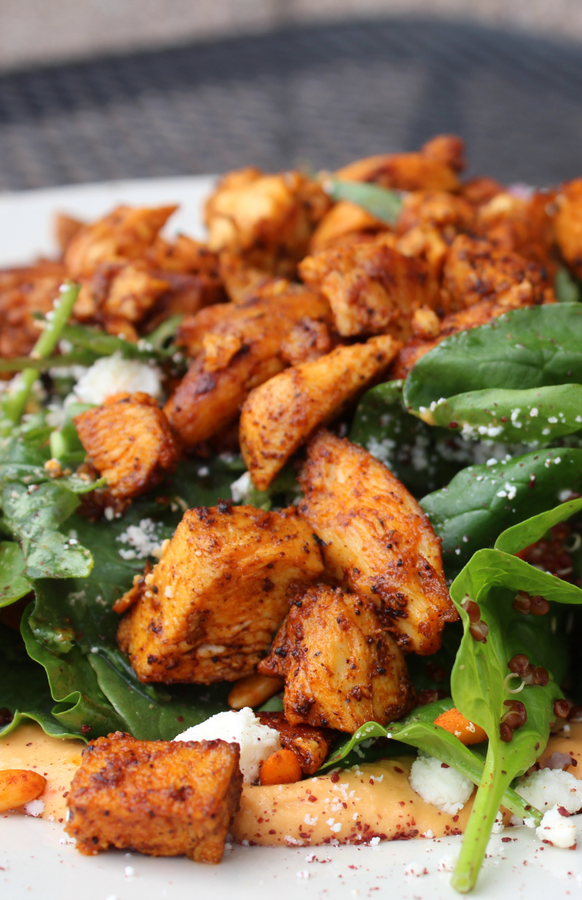 A close up of a plate of food with chicken and spinach on a table.