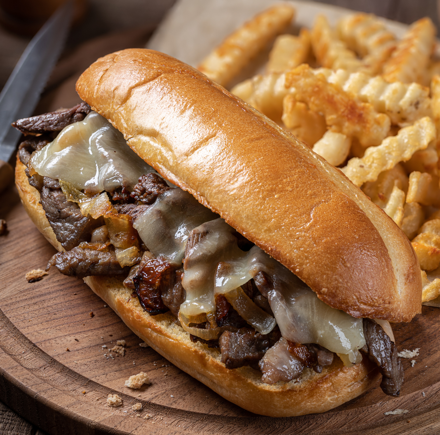 A sub sandwich with french fries on a wooden cutting board.
