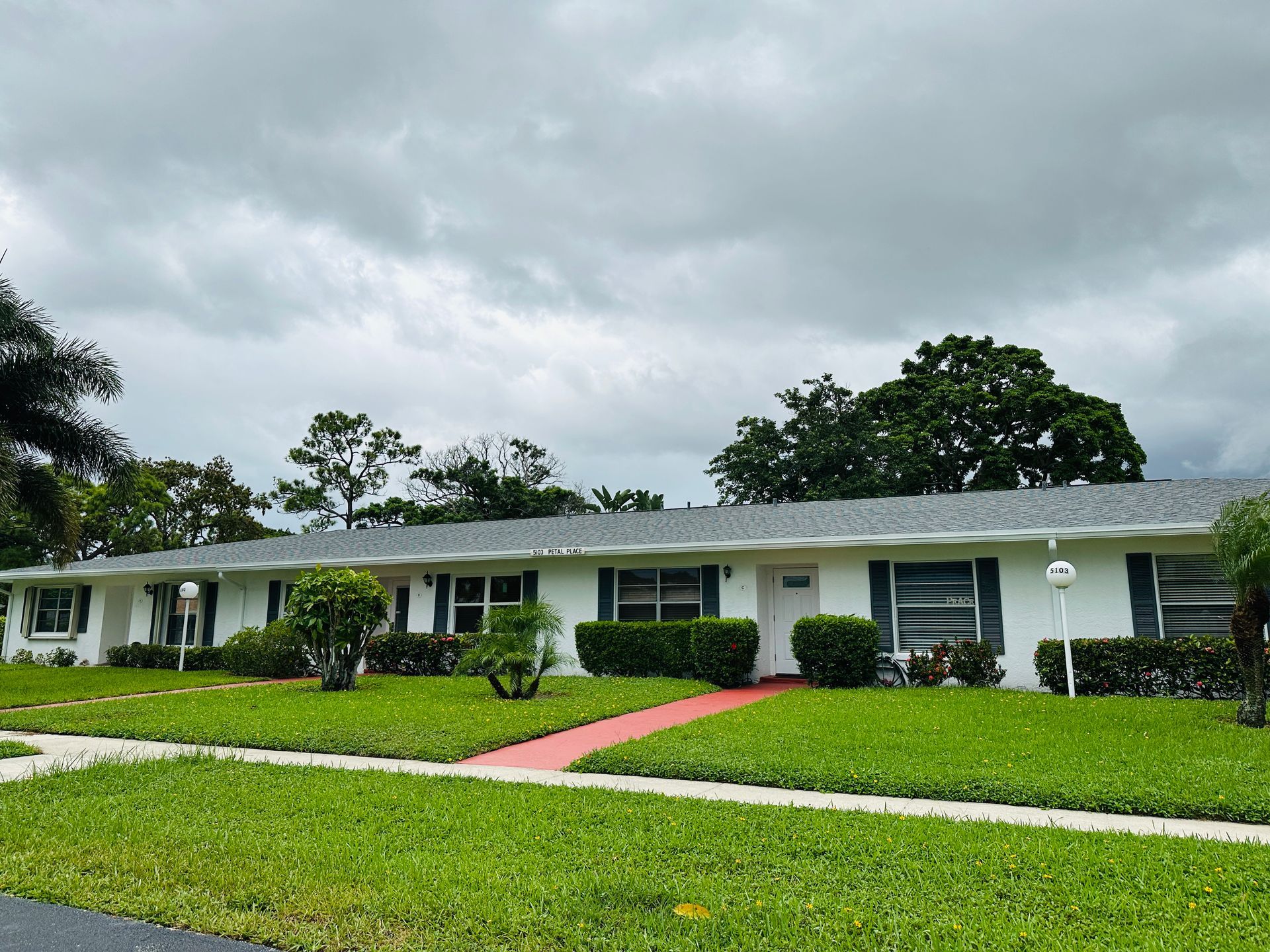 Row of white houses with green lawns and red walkways under a cloudy sky.