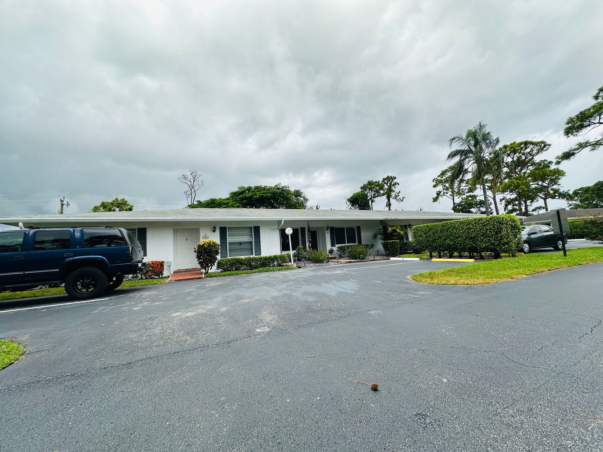White ranch-style house with dark driveway, dark blue SUV parked in front, cloudy sky.