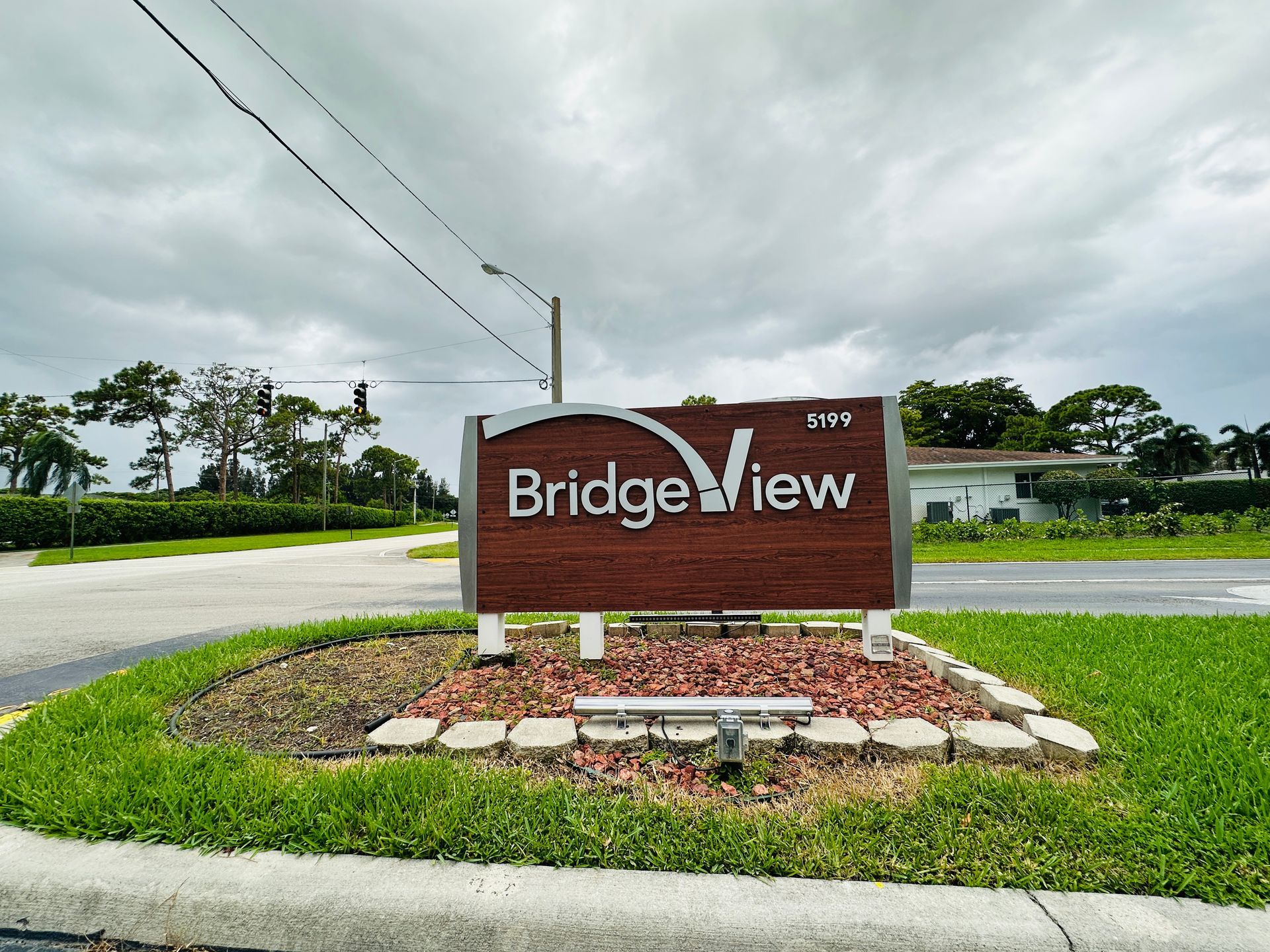 Bridgeview community sign, brown with white lettering, on a landscaped island, overcast sky.