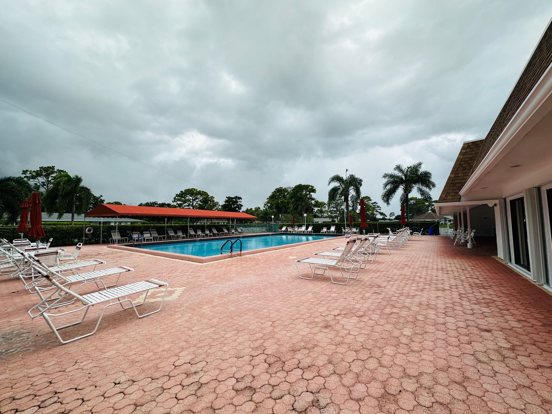 Pool with lounge chairs under a cloudy sky. Building on the right.