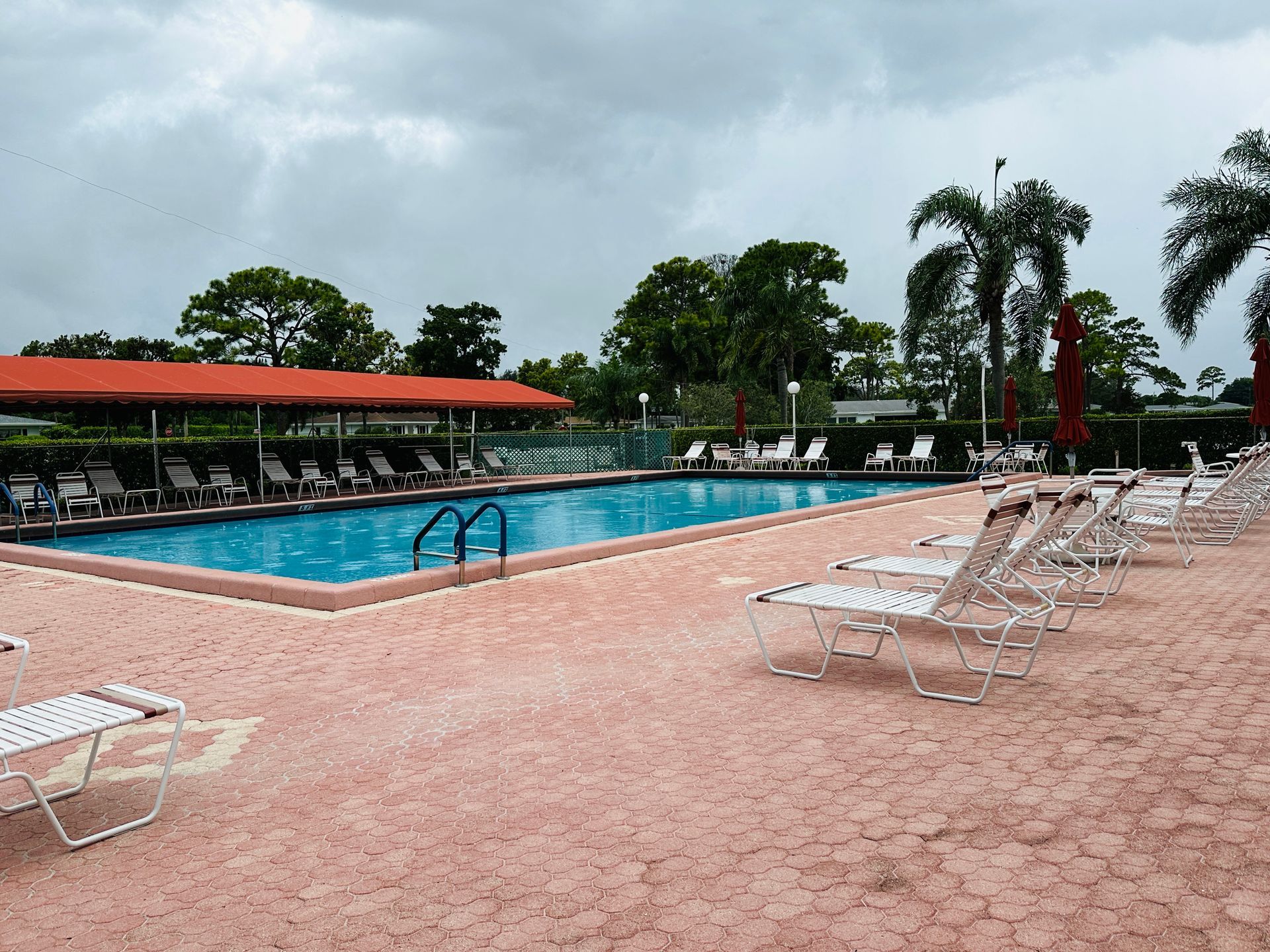 Swimming pool with empty lounge chairs and an overcast sky.