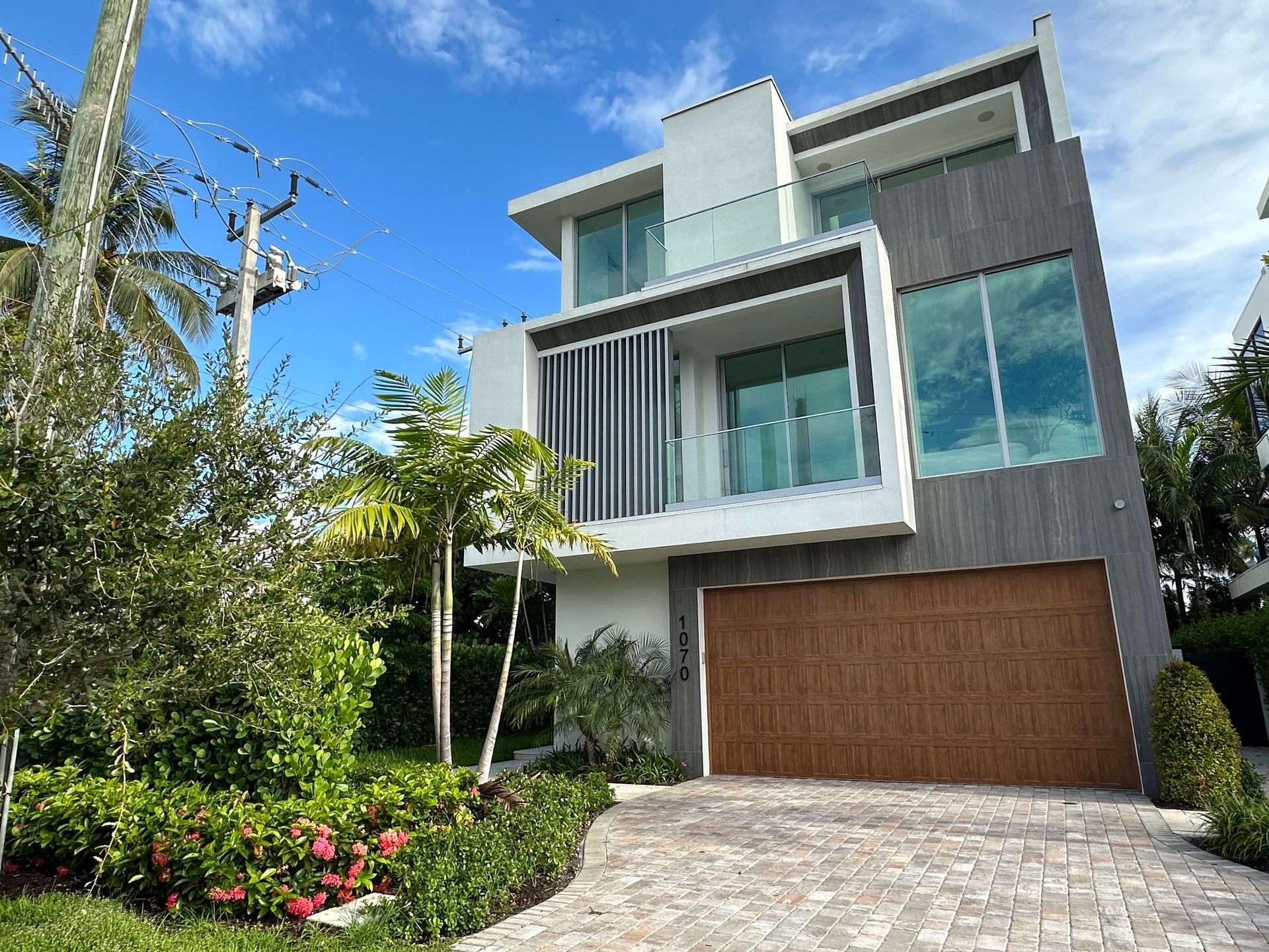 Modern multi-story house with grey facade, brown garage door, large windows, blue sky.