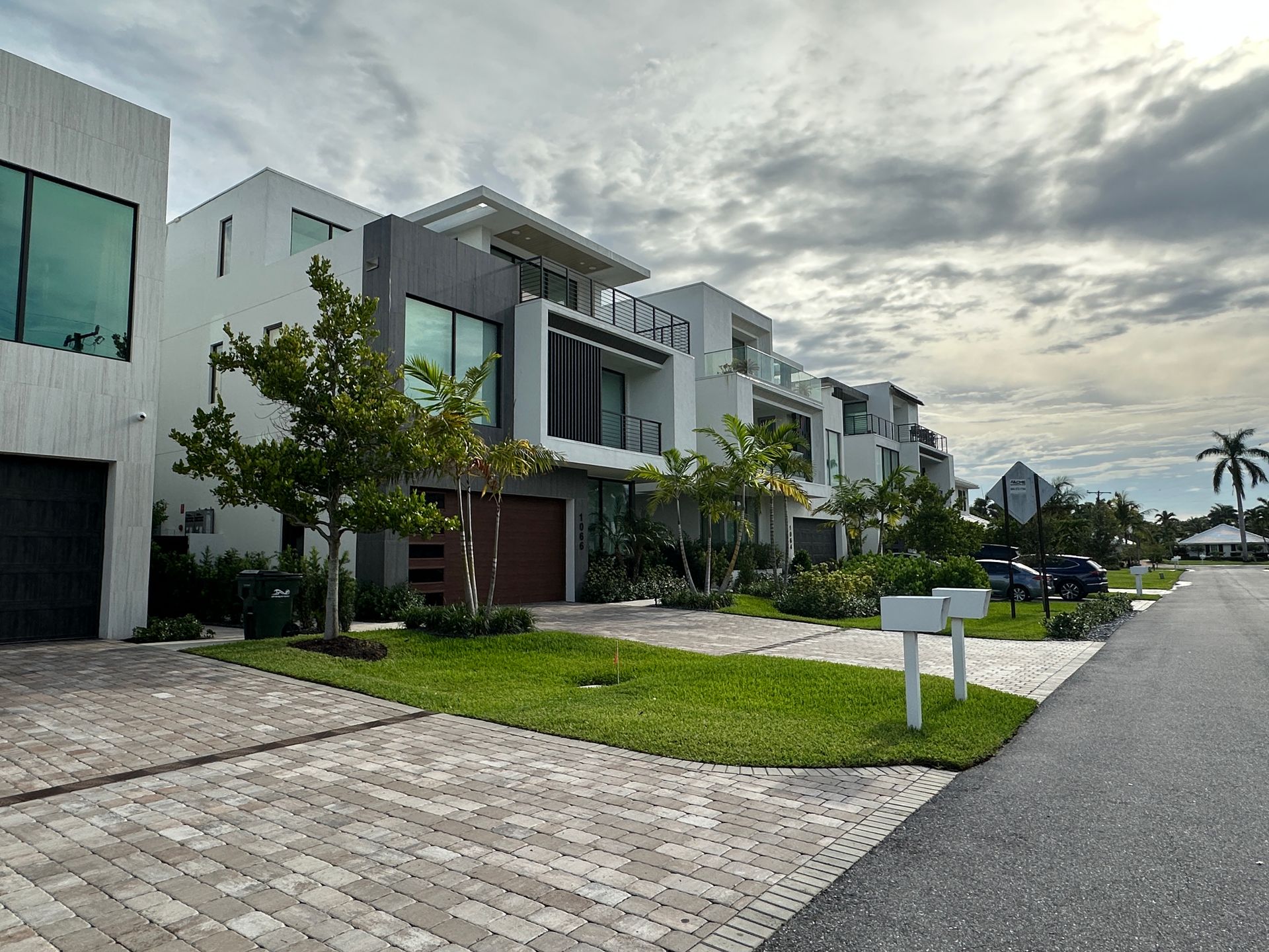 Modern multi-story houses with manicured lawns and a street on a cloudy day.