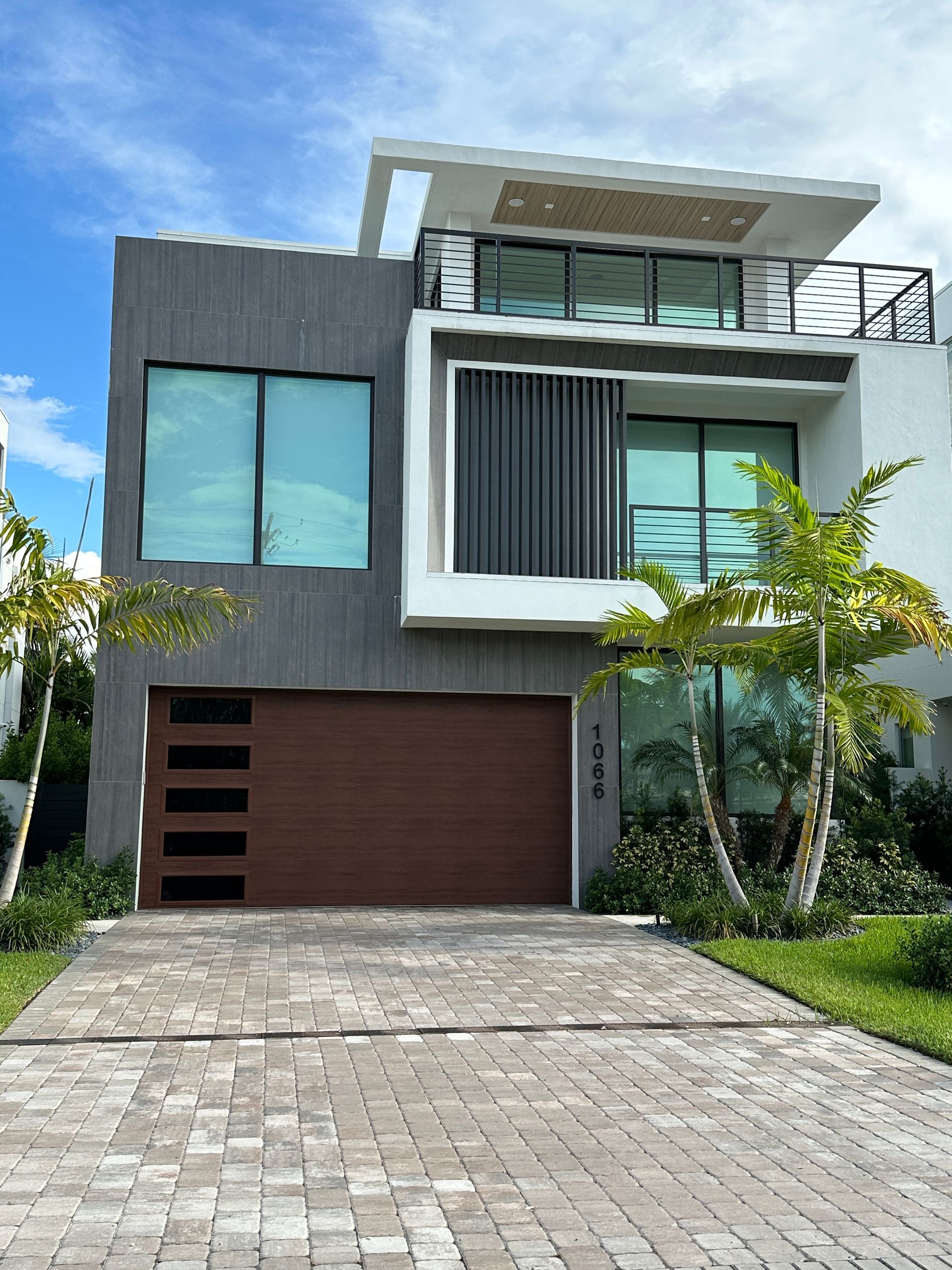 Modern gray and white house with a brown garage door and a brick driveway.