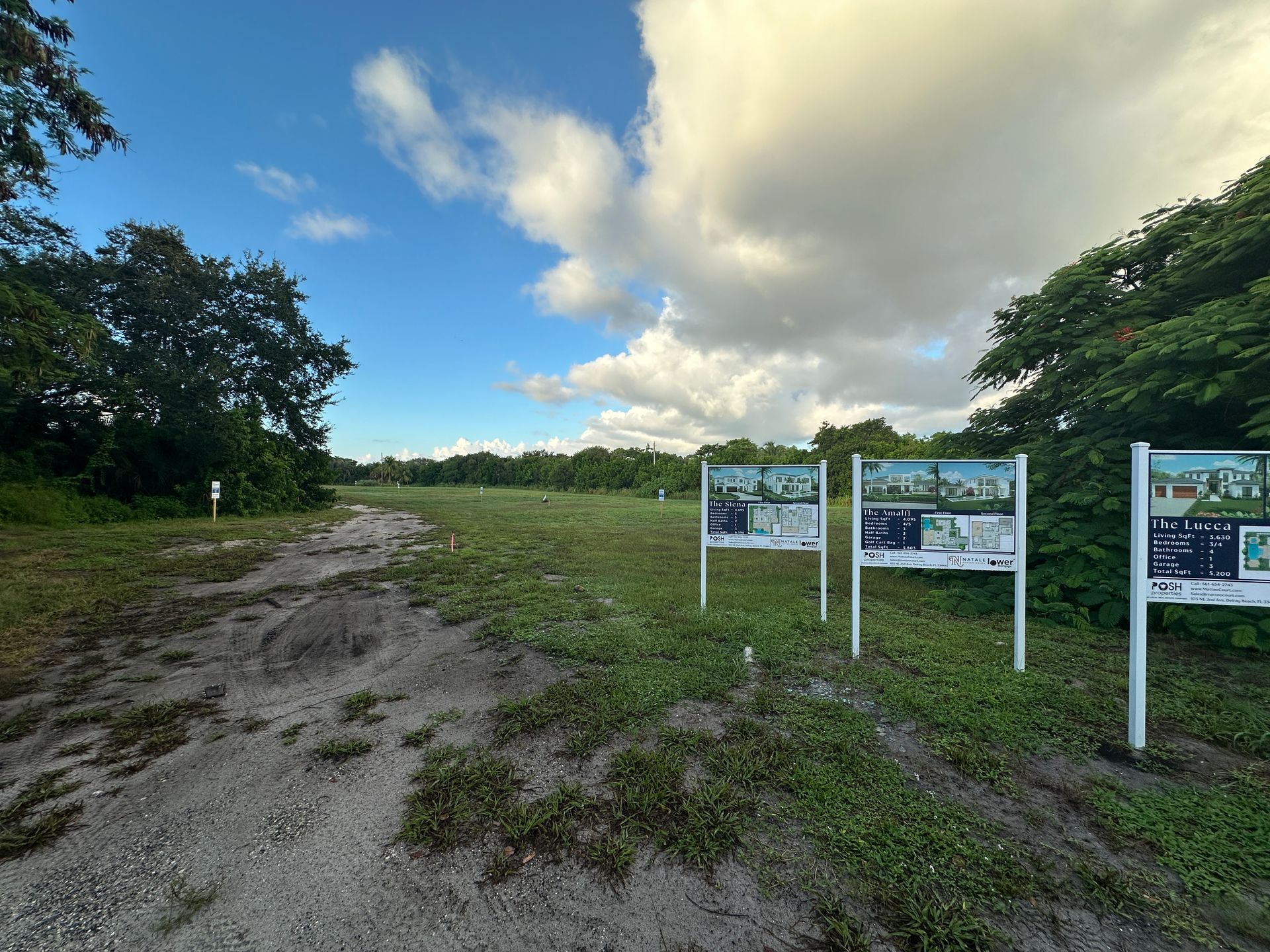 Open field with informational signs, blue sky, and scattered clouds.