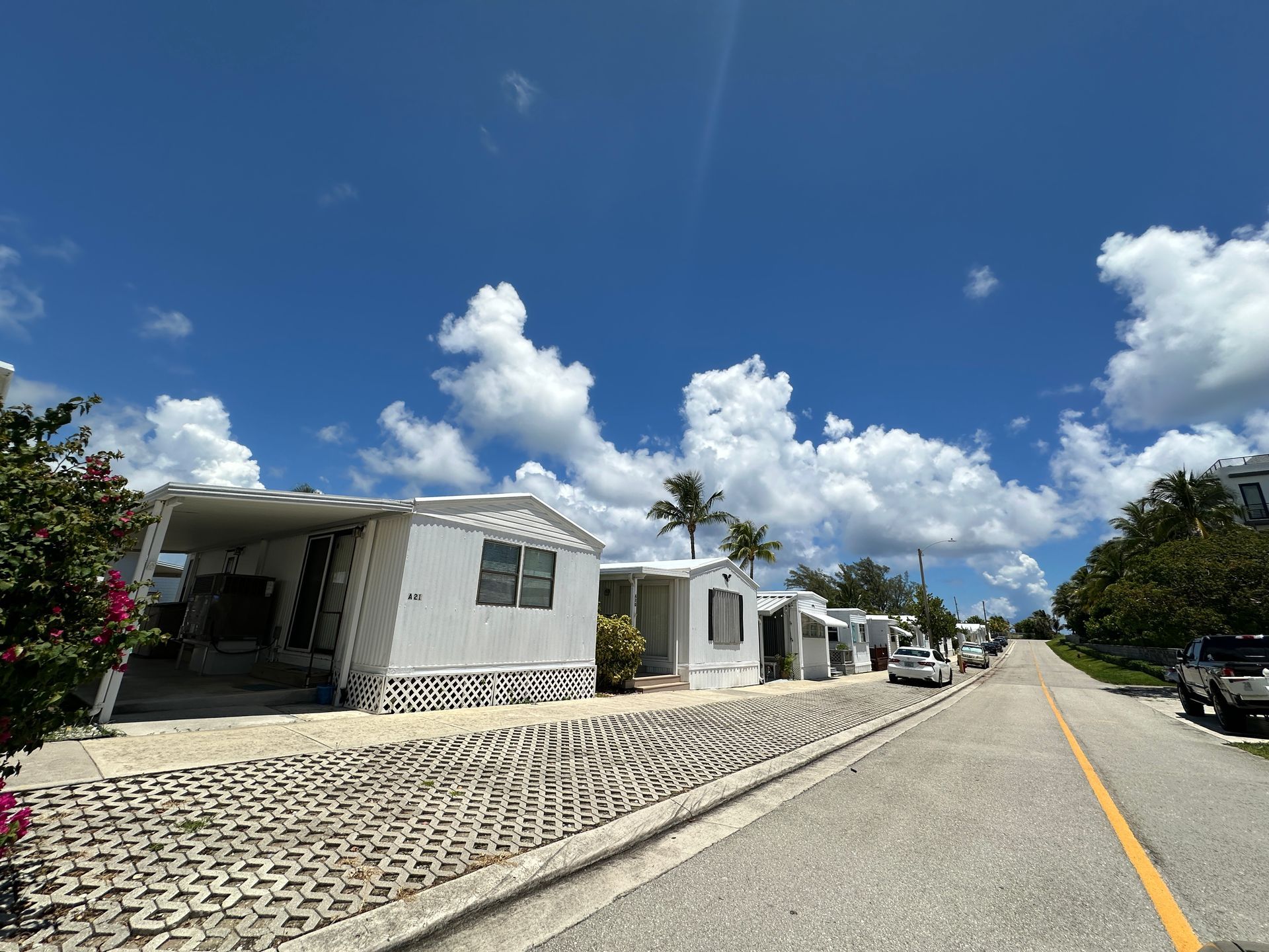 Mobile homes line a street under a blue sky with puffy white clouds.