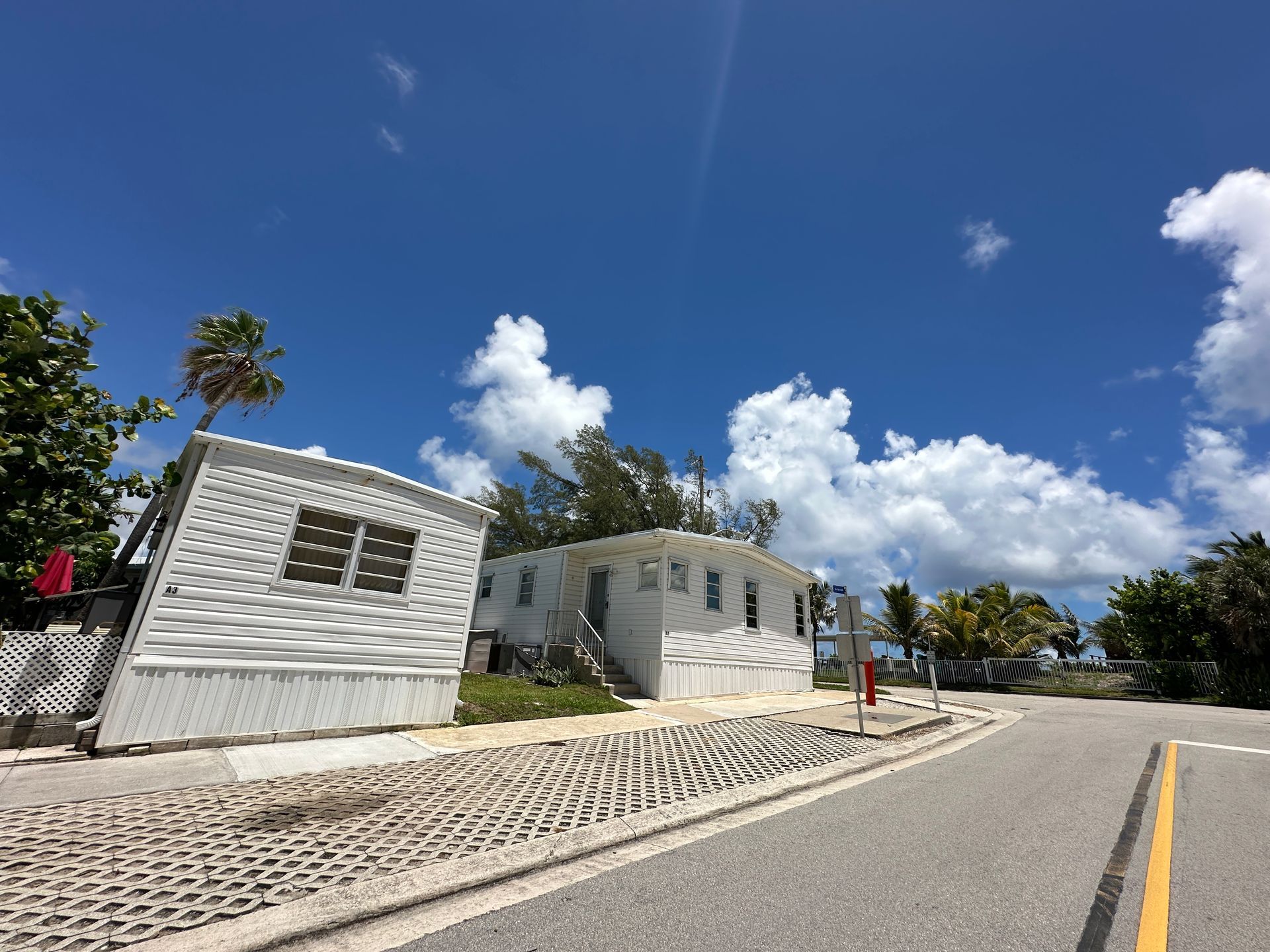 White buildings with a blue sky and fluffy clouds beside a road.